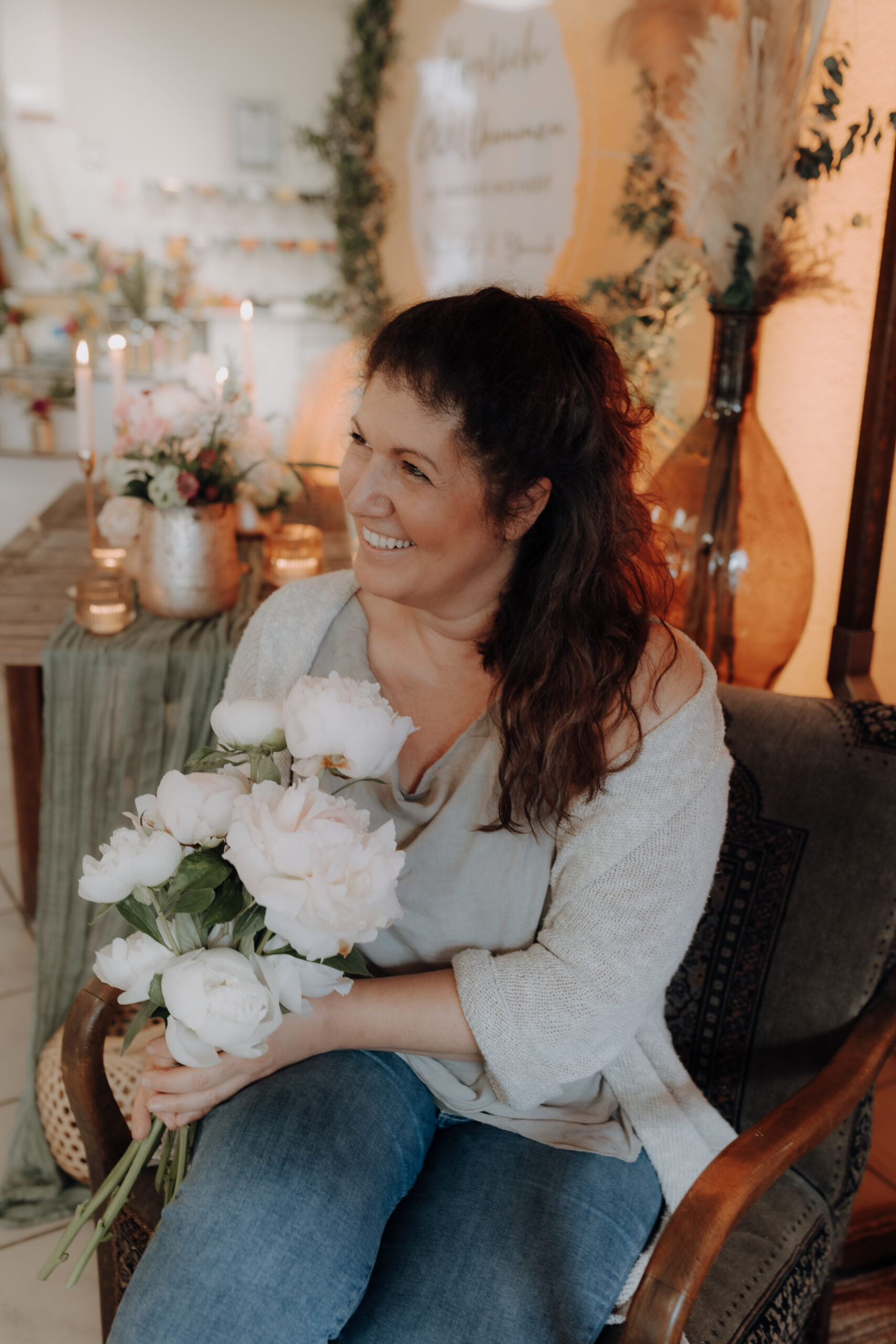 Tanja Spaniol-Schnur auf einem Stuhl sitzend, mit einem Strauß weißer Blumen in einem warm dekorierten Raum mit eleganter Blumendeko - perfekt für besondere Veranstaltungen im Saarland.