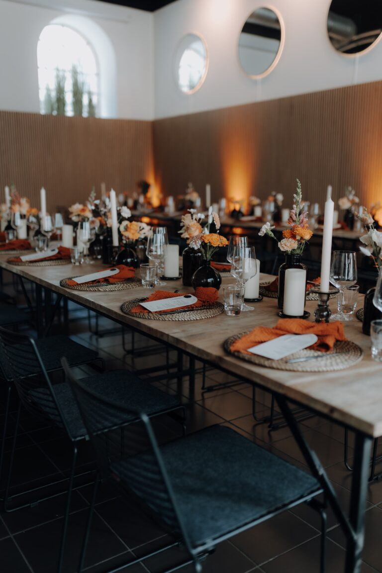 Eleganter Esstisch mit Blumen, Kerzen und orangefarbenen Servietten in einem warm beleuchteten, modernen Raum - perfekt für die Hochzeitsplanung oder besondere Anlässe in Luxemburg, mit atemberaubender Blumendeko.