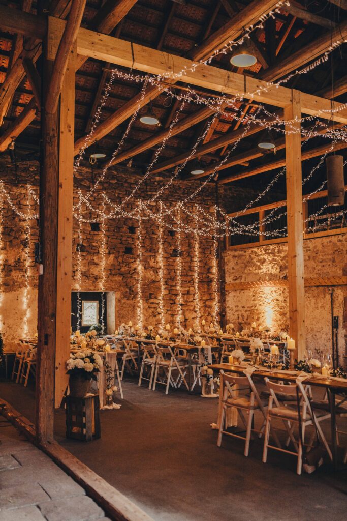 Eine rustikale Scheune, geschmückt mit Lichterketten und mit langen Tischen und Stühlen für eine Veranstaltung oder Hochzeit ausgestattet, die an das charmante Ambiente der Hochzeitslocation Forsthaus Neuhaus erinnert.