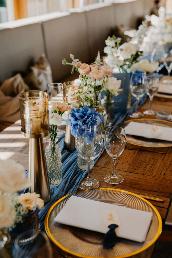 Eine elegante Tischdekoration mit blau-weißen Blumen, goldgerahmten Tellern und goldenen Kerzenhaltern – perfekt für eine Feier in der Hochzeitslocation Forsthaus Neuhaus.