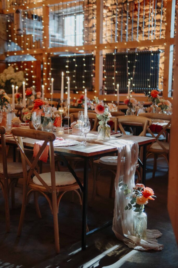 Ein rustikaler Tisch mit Blumen, Kerzen und Lichterketten in einem warm beleuchteten, festlich geschmückten Veranstaltungsraum – die perfekte romantische Kulisse in der Hochzeitslocation Forsthaus Neuhaus.